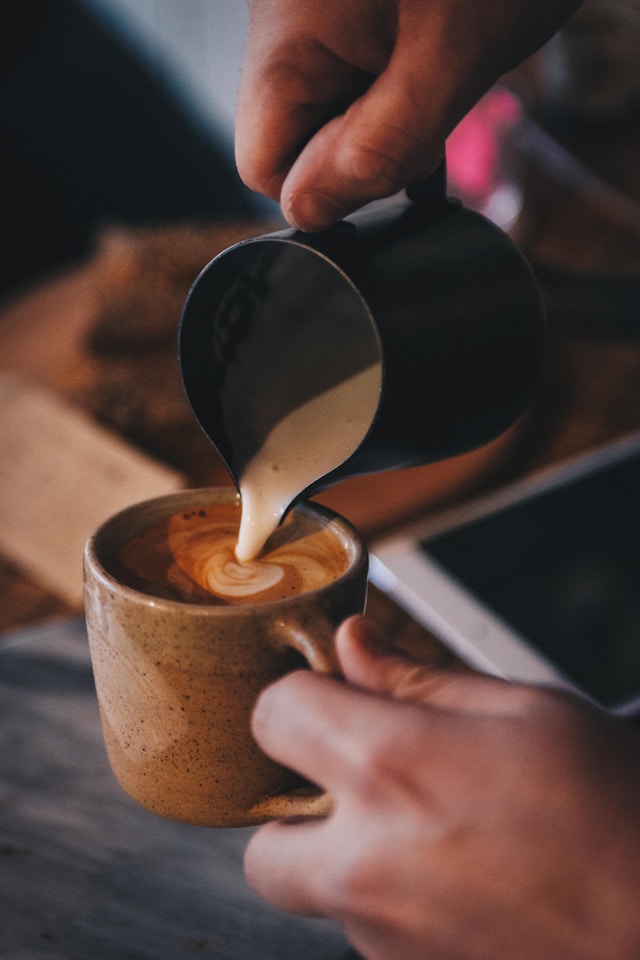 Un barista care toarna lapte spumat intr-o cana care exemplifica cum se face capucino